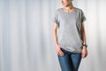 Front view of young woman, dressed in light gray t-shirt and blue jeans, standing on light gray background Royalty Free Stock Photo