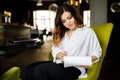 Front view. Young woman sits in cafe at a table, holding pen, reading documents. A businesswoman signs a contract. Startup, Royalty Free Stock Photo