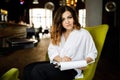 Front view. Young woman sits in cafe at a table, holding pen, reading documents. A businesswoman signs a contract. Startup, Royalty Free Stock Photo