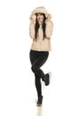 Front view of a young woman in winter jacket with a hood, and black jeans posing on a white background Royalty Free Stock Photo