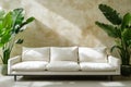 In front of a wall that features a plant and a vase, there is a couch that is white in color Royalty Free Stock Photo