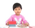 In front of the white background, the little girl is playing with the coins on the table and the model of the small house Royalty Free Stock Photo