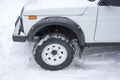 Front winter snow-covered wheel of white SUV on white beautiful drive with the front of the car