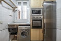 Frontal image of Kitchen with light wood furniture and column of stainless steel appliances with refrigerator and washing machine Royalty Free Stock Photo