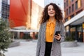 Frontal portrait of a attractive young woman portrait outdoors with phone in hand, at the modern building background.