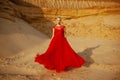 Beauty portrait of a sensual young blonde woman, wear in red long flying dress, posing in a sand desert.