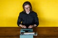 A man in black shirt, working on manual typewriter, seated at wooden table, over yellow background. Copy space. Royalty Free Stock Photo