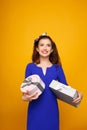 Cheerful girl in blue dress holding heap of presents, looking up,  on yellow background. Copy space. Royalty Free Stock Photo