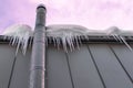 Frosted chimney pipe and icicles hanging from eaves of roof on cold day in dramatic sky background