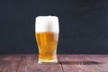 A frosted glass of light beer with a frothy cap on a wooden table Royalty Free Stock Photo