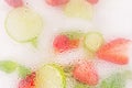 Frosted Glass with water drops with fruits behind it. Close-up of refreshing cocktail