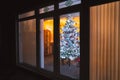 A frosted white artificial christmas tree with red and silver decorations seen through large patio doors with vertical slat blinds