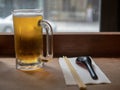 Frosty beer mug filled with lager on table with chopsticks and soup spoon