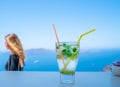 Frosty glass with mojito drink in focus in foreground with person in background out of focus