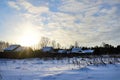 frosty winter morning in countryside. Sun peeks out from behind roofs of houses. Everything is covered with snow Royalty Free Stock Photo