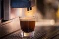 A frothy aromatic fresh coffee being poured from coffee machine into a glass mug