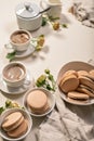 Frothy coffee in white cups, delicious French macaroons. Dessert still life on a beige background. Vertical shot Royalty Free Stock Photo