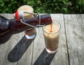 Frothy dark beer pouring into tall glasses from a brown glass bottle in summer garden on rustic wooden table