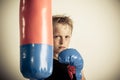 Frowning blond boy stands beside punching bag Royalty Free Stock Photo