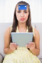 Frowning brunette with credit card on forehead holding tablet