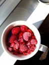 Frozen berries raspberries in hot water in mug on window background