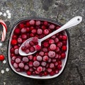 Frozen cranberries in a white enameled vintage bowl on a plain gray background with a beau enameled spoon. Top View.