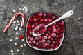 Frozen cranberries in a white enameled vintage bowl on a plain gray background with a beau enameled spoon. Top View.