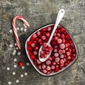 Frozen cranberries in a white enameled vintage bowl on a plain gray background with a beau enameled spoon