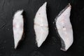 Frozen fillets of white fish, pollock, on black dark stone table background, top view flat lay