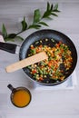 Frozen fried vegetables on black pan. Vegan breakfast with juice. Vegetables food mix on white wooden background with plant Royalty Free Stock Photo