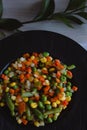 Frozen fried vegetables on black plate. Vegan breakfast. Vegetables food mix on white wooden background with plant Royalty Free Stock Photo