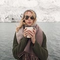 Frozen girl holds a cup of hot coffee. Mountain lake