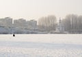 Frozen lake in the city with the fisherman on the background of houses and churches.