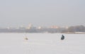 Frozen lake in the city with the fisherman on the background of houses and churches.