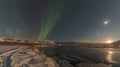 A frozen lake lies undisturbed reflecting the moon and the Northern Lights above creating a serene and solitary