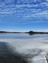 Frozen lake or sea melting in the spring. Blue sky with unusually shaped soft clouds and forested islands in the distance. Finnish Royalty Free Stock Photo