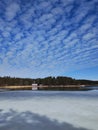 Frozen lake or sea melting in the spring. Blue sky with unusually shaped soft clouds. Houses, buildings, maybe summer cottages on Royalty Free Stock Photo