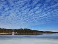 Frozen lake or sea melting in the spring. Blue sky with unusually shaped soft clouds. Houses, buildings, maybe summer cottages on Royalty Free Stock Photo