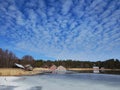 Frozen lake or sea melting in the spring. Blue sky with unusually shaped soft clouds. Houses, buildings, maybe summer cottages on Royalty Free Stock Photo