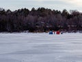 Ice fishing; Frozen lake surface in winter with two ice shanties or huts and a fisherman in between them. Royalty Free Stock Photo