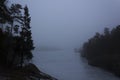 Frozen lake surrounded by small mountains with pine and fir trees on a misty morning. Nackareservatet - nature reserve in Swed