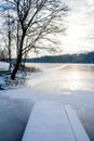 Frozen lake in winter, with pier, wooden boats and trees covered by snow Royalty Free Stock Photo