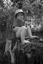 A frozen little girl sits on a stump barefoot. Black and white image