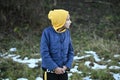Frozen little thin caucasian girl in yellow hoodie and blue jacket shiver near snow on ground in outdoor park during leisure