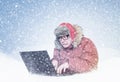 Frozen man in red winter clothes working on a laptop in the snow. Cold, frost, blizzard