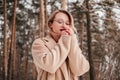Frozen mid age woman in winter forest warming up hands outdoors looking down. Blonde girl in coat sweater and eyeglasses