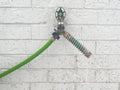 Frozen outdoor water spigot on white brick wall background with long ice dripping from garden hose protector coil spring