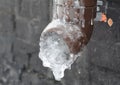 A frozen rain gutter downpipe. Ice inside the downspout, downpipe of a roof gutter near the house foundation causing damage to the