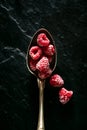 Frozen raspberries on a spoon, black stone background
