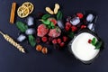 Frozen raspberry, blackberry, strawberries, yoghurt plate mint leaves, pieces of ice on a black shale board, slices of lemon, nuts Royalty Free Stock Photo